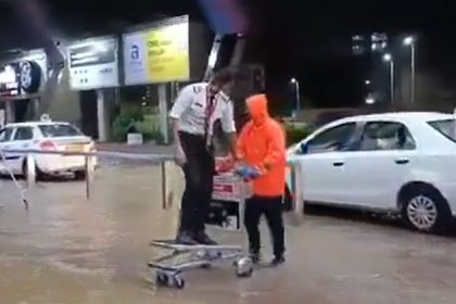 Pilot at Jaipur airport rides atop luggage trolley to cross waterlogged ariport entrance.