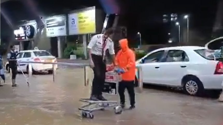 Pilot at Jaipur airport rides atop luggage trolley to cross waterlogged ariport entrance.